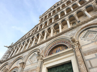 Fototapeta premium A detailed close-up of the ornate facade of the Pisa Cathedral, showcasing exquisite Romanesque architecture, decorative arches, and intricate stone carvings under a clear blue sky.