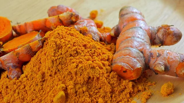 Turmeric root and turmeric powder on wooden plate.