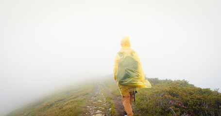 Back view of woman hiker exploring nature in a misty rainy landscape. Mountains in the foggy weather.
