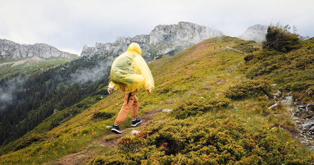 Woman in yellow waterproof coat hiking admiring the mountains cliffs. Back view of female hiker...