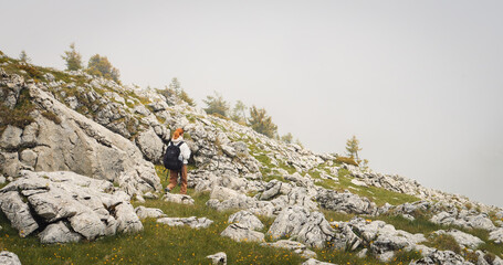 Naklejka premium Caucasian girl walking on a rocky hiking path in a hoodye and wearing a backpack. Leisure travelling concept.