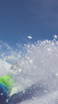 SLOW MOTION TIME WARP, CLOSE UP: Extreme male snowboarder riding off piste crashes into powder snow. Freeride snowboarder on adrenaline filled ride down sunny mountain falls into freshly fallen snow