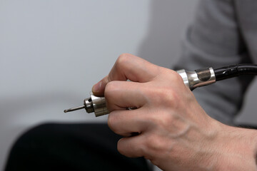 A drill press with a drill bit in the hands of a man close-up.
