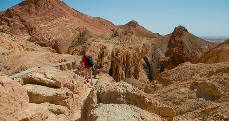 Man with backpack hiking narrow slot canyon in Sahara going down the path. Travelling to the desert...