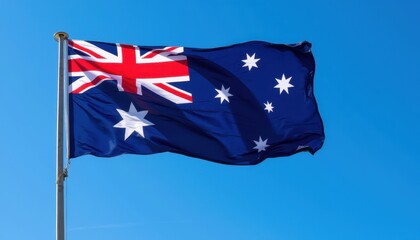 The Australian flag waves against a clear blue sky, featuring the Union Jack, a large white seven-pointed star, and five smaller white stars representing the Southern Cross constellation