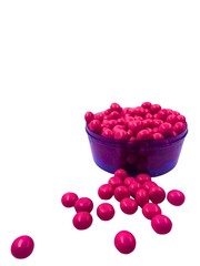 A shallow purple bowl is brimming with round, glossy pink candies. A few candies have spilled out,...