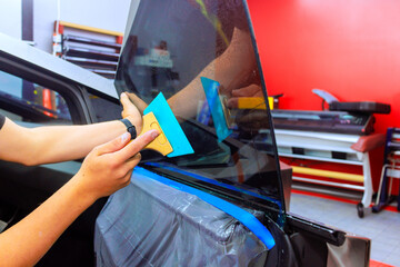 Technician carefully applies window tint film to car door in well it auto workshop using squeegee.