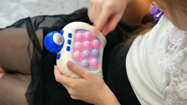 The hands of a little girl playing electronic Pop It, presses on the bubbles illuminated with red light. Trains mindfulness. A modern children's toy.