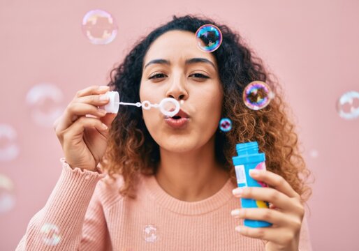 Young woman having fun blowing soap bubbles on a pink background