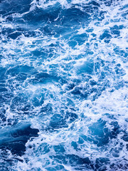 Fototapeta premium Powerful ocean waves crashing against dark rocks, creating white foam and intricate water patterns under natural light