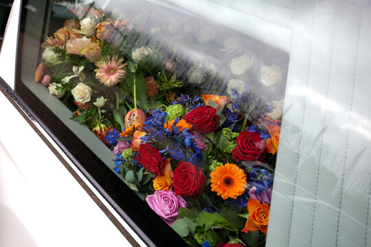 Bloemen met kruis achter glas van een rouwauto tijdens een begrafenis