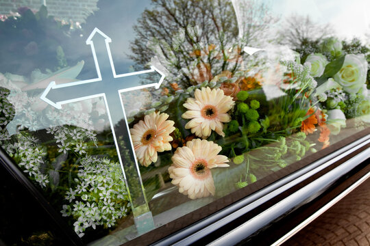 Bloemen met kruis achter glas van een rouwauto tijdens een begrafenis