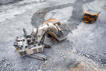 Open pit mining industry, aerial top view. Industrial excavator loading ore into big yellow truck...