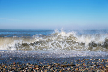 Waves roll to the pebble shore under a blue sky
