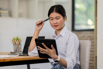 Obraz premium Young modern business asian woman working using digital tablet while sitting in the workplace office
