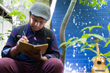 a latino man poet sitting in the garden next to a guitar writing poetry in a book