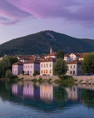 Fototapeta premium Riverside Town with Forested Mountains Under Vibrant Evening Sky