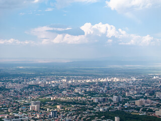 Fototapeta premium Cityscape in summer. Beautiful clouds on the sky. City near the mountains. Top view, drone photo.