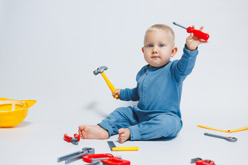 Baby boy on a white background plays with a plastic hammer. Children's set of tools for...