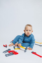 Baby boy on a white background plays with a plastic hammer. Children's set of tools for construction. Child plays with toys on a white background