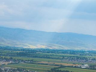 Fototapeta premium Mountain landscape in summer before the rain. The sun rays break through the clouds. Village near the mountains. Top view, drone photo.