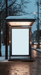 Snow-covered bus stop in a city at night. White billboard illuminated by light, traffic lights, cars moving. Winter setting with snow-covered trees, peaceful scene on well-lit street.