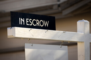 A sign stating In Escrow with a house in the background