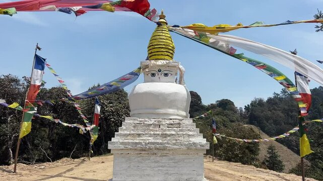 A Buddhist stupa in the nature on a trekking path. Little temple with a golden dome, the buddha's eyes on top and the traditional colourful prayer flags that waving