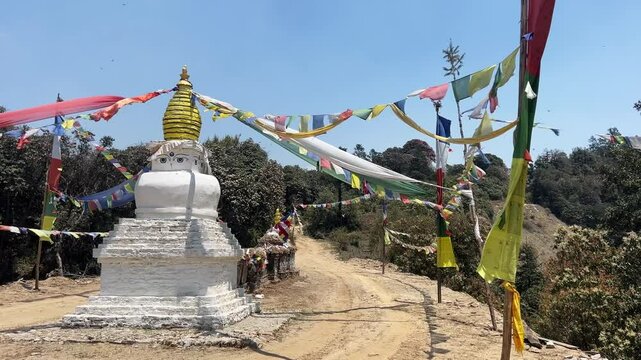 A Buddhist stupa in the nature on a trekking path. Little temple with a golden dome, the buddha's eyes on top and the traditional colourful prayer flags that waving