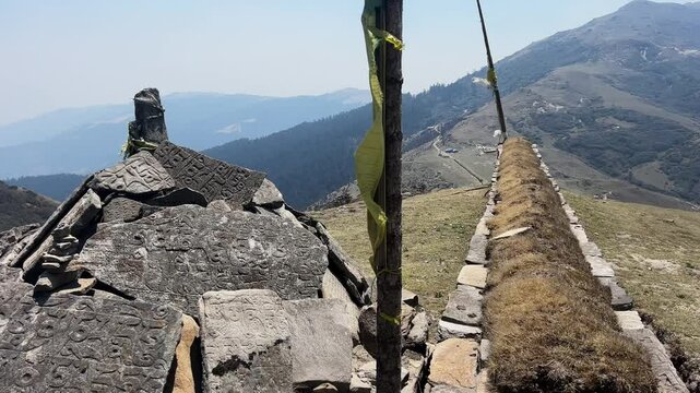 A landmark on a trekking path on the Himalayan range. There is a pole with the traditional prayer flags and a little traditional and holy little wall for the porters and people from this land