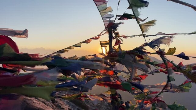 Many Tibetan Buddhist prayer flags that waving in a strong wind of a Himalayan mountain peak. in the background the sun the rise behind the range