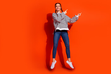 Young woman with red hair wearing a striped pullover smiles brightly against a vibrant orange...
