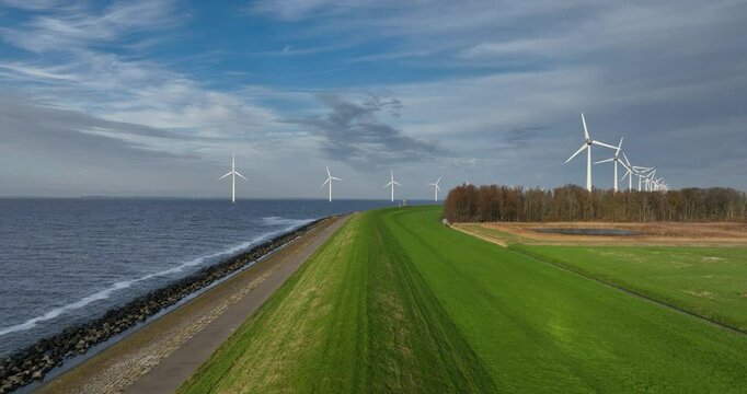 Aerial drone video of a dijk, water barrier in The Netherlands, Wind turbines at open water.