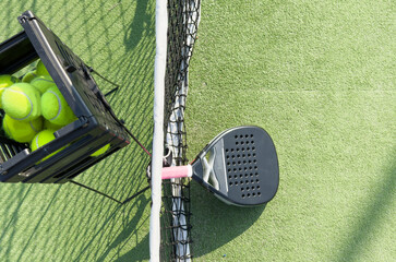  padel racket and yellow balls placed on court near net on sunny day