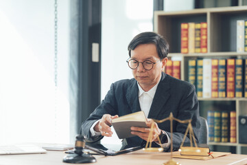 Focused Lawyer Reviewing Case Files: A meticulous Asian male lawyer in a dark suit sits at his...