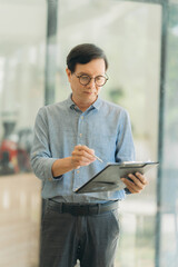 Focused Professional: A businessman in a blue shirt and glasses thoughtfully reviews a clipboard, showcasing dedication and meticulousness in his work.  