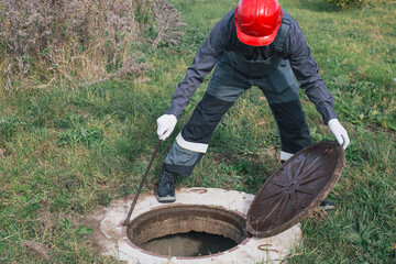 Worker opens septic well manhole cover. septic tank maintenance and sewage pumping