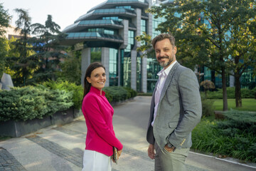 Medium shot of happy multi ethnic business couple posing in front of glass building exterior. Portrait of successful business team posing outdoor.