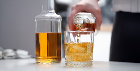 A hand pours a brown alcoholic drink into a glass, close-up, blurry. Drinking alcoholic cocktails, whiskey on ice