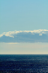 Obraz premium An enchanting view of the vast ocean under a dramatic sky with clouds forming patterns. The sun's rays pierce through, creating a golden path on the water.