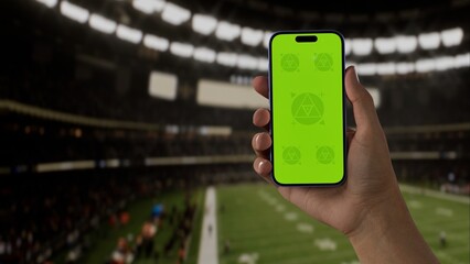 GREEN SCREEN CHROMA KEY A hand holding a phone with a green screen at an American football game in a stadium at night, perfect for showcasing live sports or betting apps