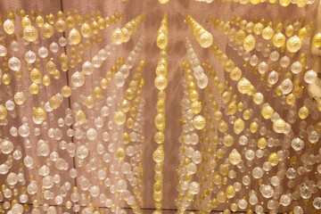 Myriads of small golden and clear glass balls hanging on threads like garlands against a light...