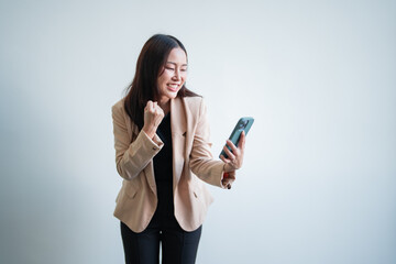 Fototapeta premium Asian businesswoman is expressing her excitement while holding a smartphone, suggesting she has just received positive news or achieved a significant milestone in her career