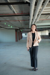Fototapeta premium Young asian businesswoman holding a smartphone and smiling in a parking garage, representing concepts of career, technology, and modern work environments
