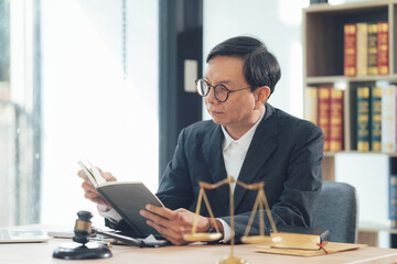 Obraz premium Lawyers office: A serious and focused lawyer in a suit, reading a legal document at his desk. The scales of justice and a gavel can be seen on the table.
