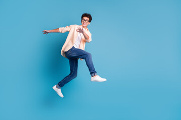 Fototapeta premium Energetic young man in trendy casual wear jumps against blue background exuding happiness and youthful style