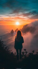 Obraz premium Contemplative young woman admiring a vibrant sunset over the ocean cliffs.