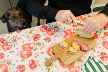 dog sitting next to the table waiting for the food that the owner is cutting