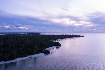 Tropical island covered in coconut palm trees, empty beach and calm ocean at twilight, aerial view