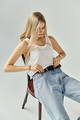A young woman with long blonde hair poses effortlessly in a stylish studio, showcasing fashion.